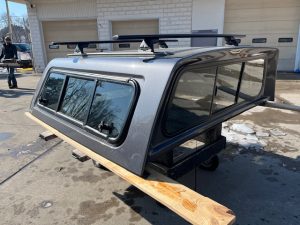 Gray truck cap with roof racks for F150, outdoor setting.