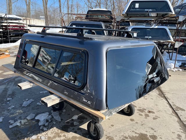 Gray truck bed camper shell for F150 with tinted windows and aerodynamic design.