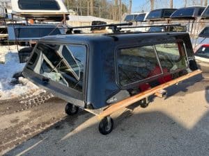 Black truck camper top with windows and wooden support, outdoor setting.