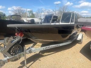 Fishing boat with black hull and dual windshields on trailer.