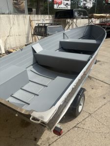 Gray utility boat with seating on trailer for fishing or recreation.