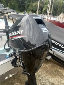 Black Mercury 25 HP outboard motor on boat with boats in background.