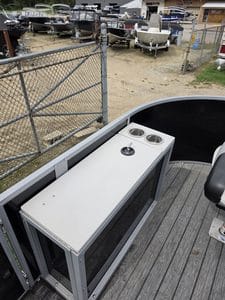 Pontoon boat with built-in cup holders and storage, docked at a marina.
