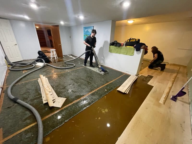 Technicians perform water extraction on a flooded basement floor.