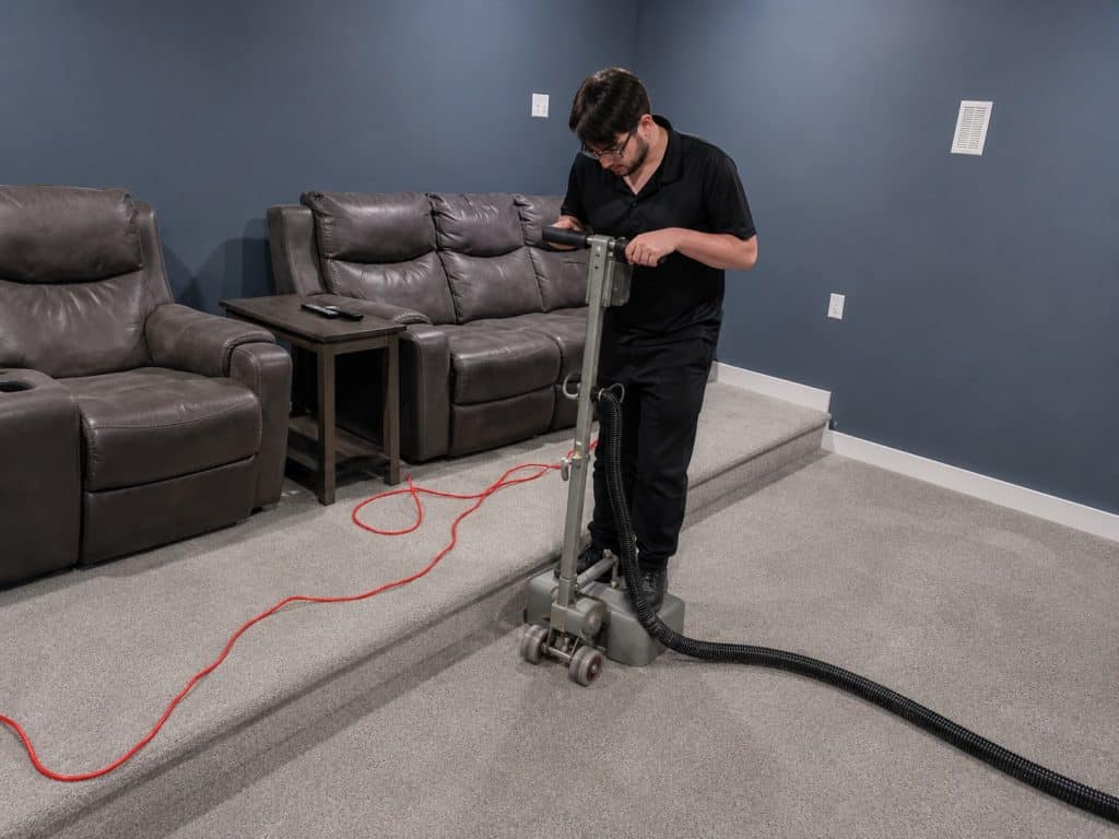 Technician performing water extraction on carpet with professional equipment.