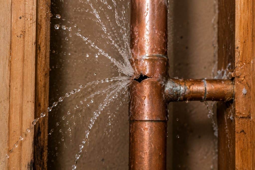 Copper pipe with water leak and spray in a wall cavity.