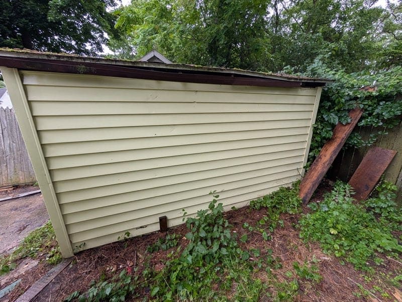 Cleaned beige siding of a small building with surrounding greenery.