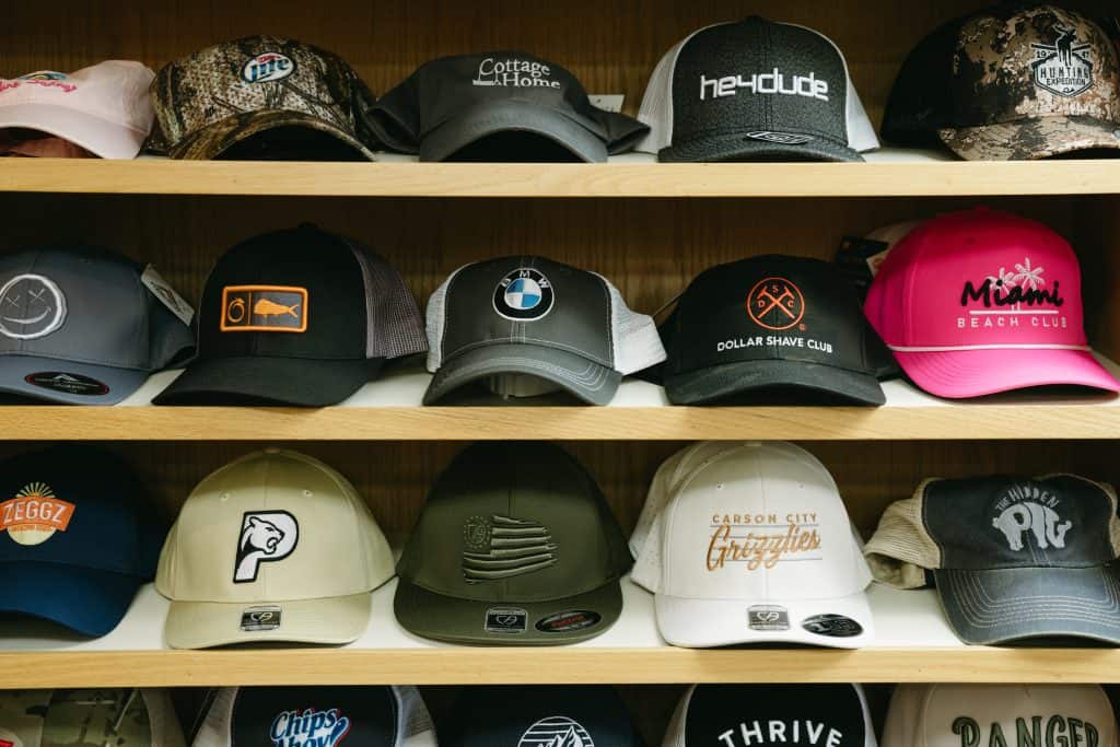 Collection of various branded caps on wooden shelves for sale or display.