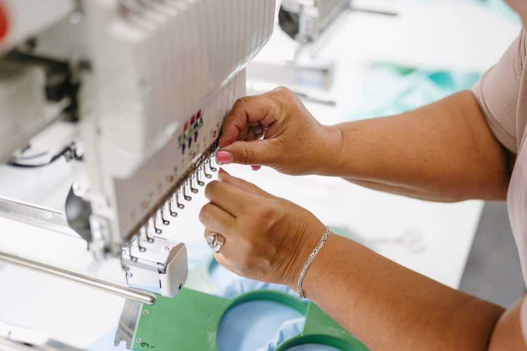 Person working on embroidery machine for website branding customization.