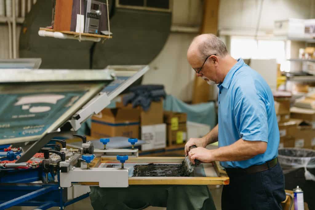 Man working on a printing or manufacturing machine in a workshop.