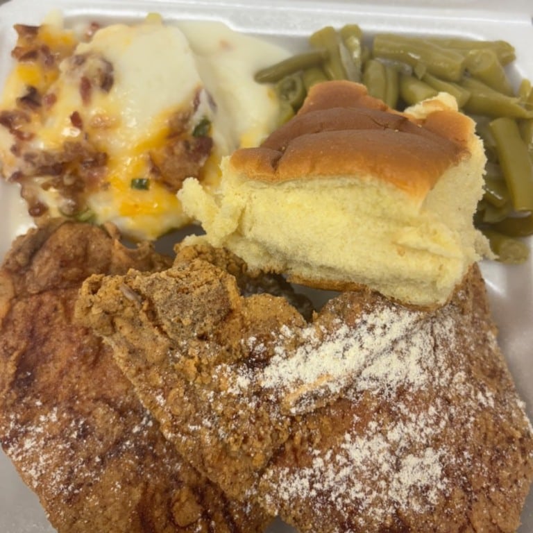 Delicious fried or smothered pork chop served with green beans, mashed potatoes, and a soft bread roll, showcasing authentic Southern soul food cuisine.