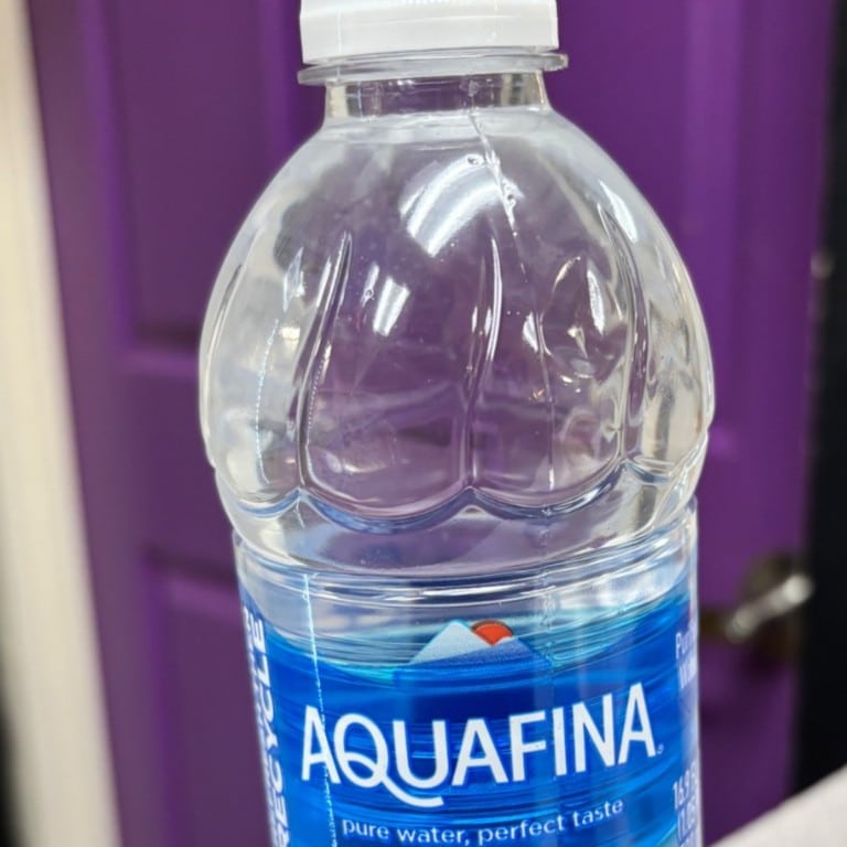 Clear plastic bottle of Aquafina bottled water with purple background.