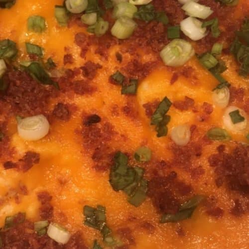 Close-up of loaded mashed potatoes topped with melted cheese, crispy bacon bits, chopped green onions, and seasoning, served as a hearty side dish.