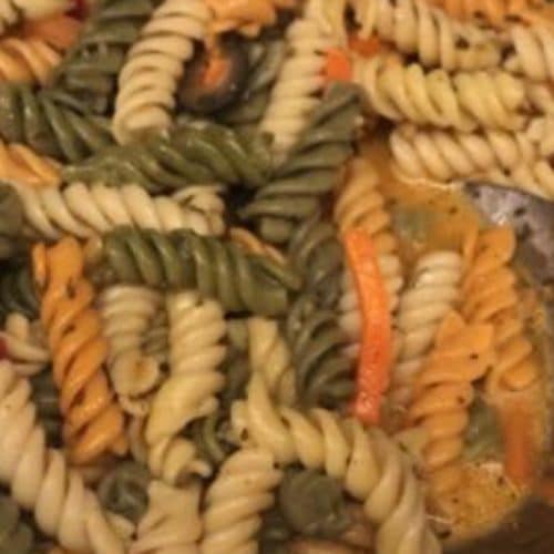 Colorful pasta salad featuring tri-color rotini, fresh vegetables, and herbs, perfect for a flavorful side dish or light meal.