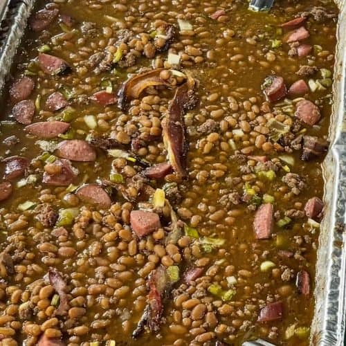 Hearty baked beans with smoked sausage and seasonings in a baking dish, showcasing Corine's Soul Food, Cakes & Catering.