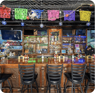 Vibrant bar with colorful papel picado decorations and a well-stocked wooden bar.