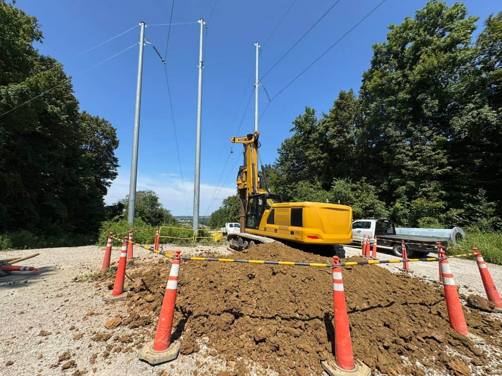 Utility pole installation at a construction site with heavy machinery and safety cones.
