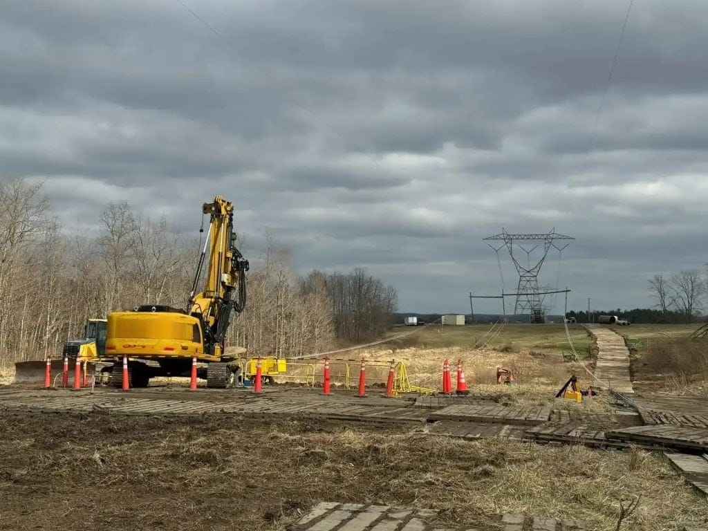 Storm damage repair at 765kV power line site with heavy machinery and safety cones.