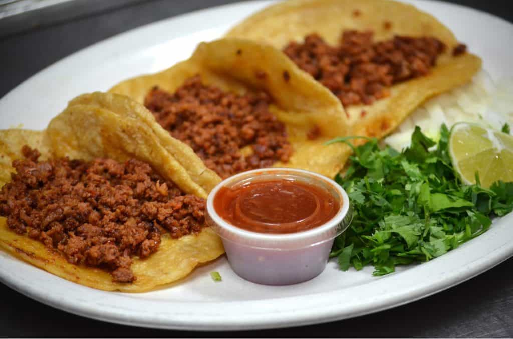 Delicious ground beef tacos with fresh cilantro, lime, and salsa on a white plate.