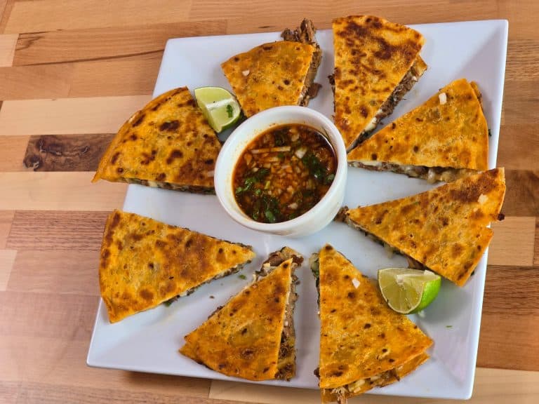 Quesadilla slices with dipping sauce and lime wedges on a white plate.