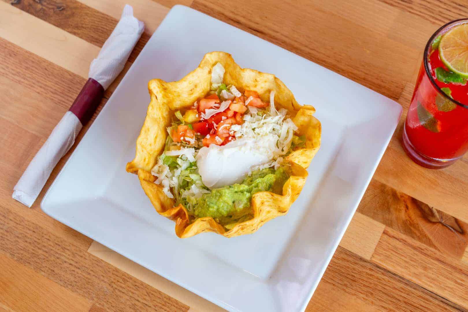 Tacos served in a crispy tortilla bowl with guacamole, sour cream, and fresh vegetables.
