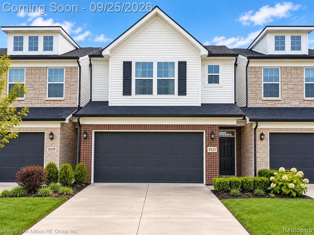 Contemporary townhome featuring a brick and siding exterior, dormer windows, attached garages, and a paved driveway