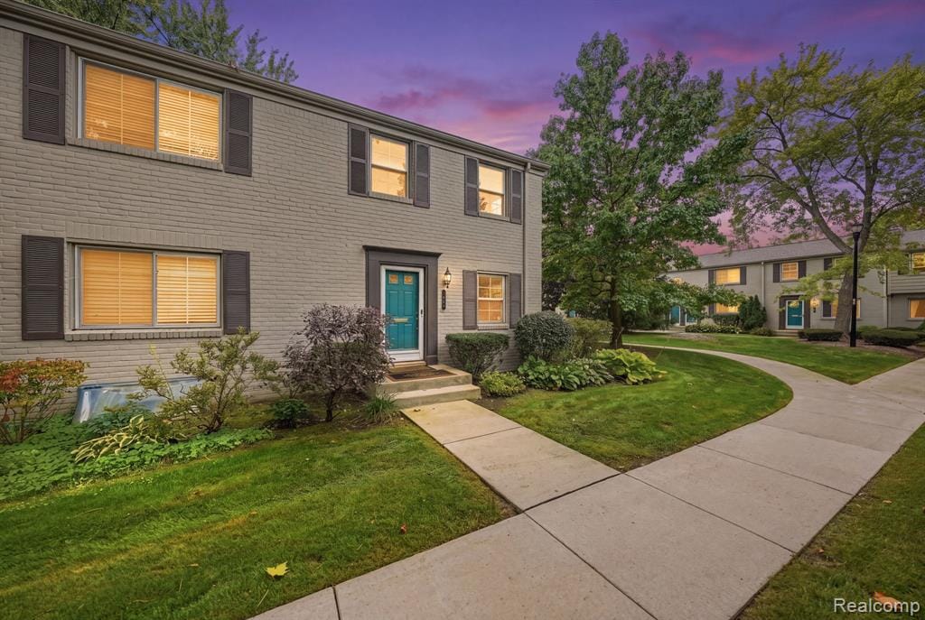 Brick exterior with dark shutters, vibrant turquoise entry door, established landscaping, and a concrete walkway
