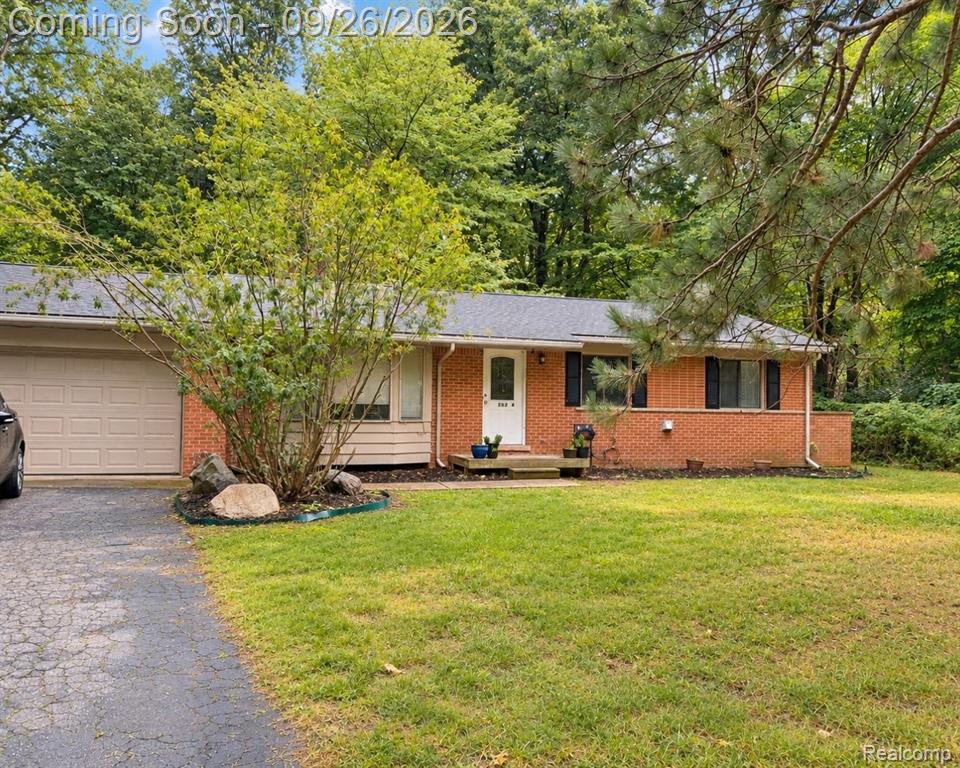 Brick exterior with black shutters, attached garage, front lawn, and mature trees