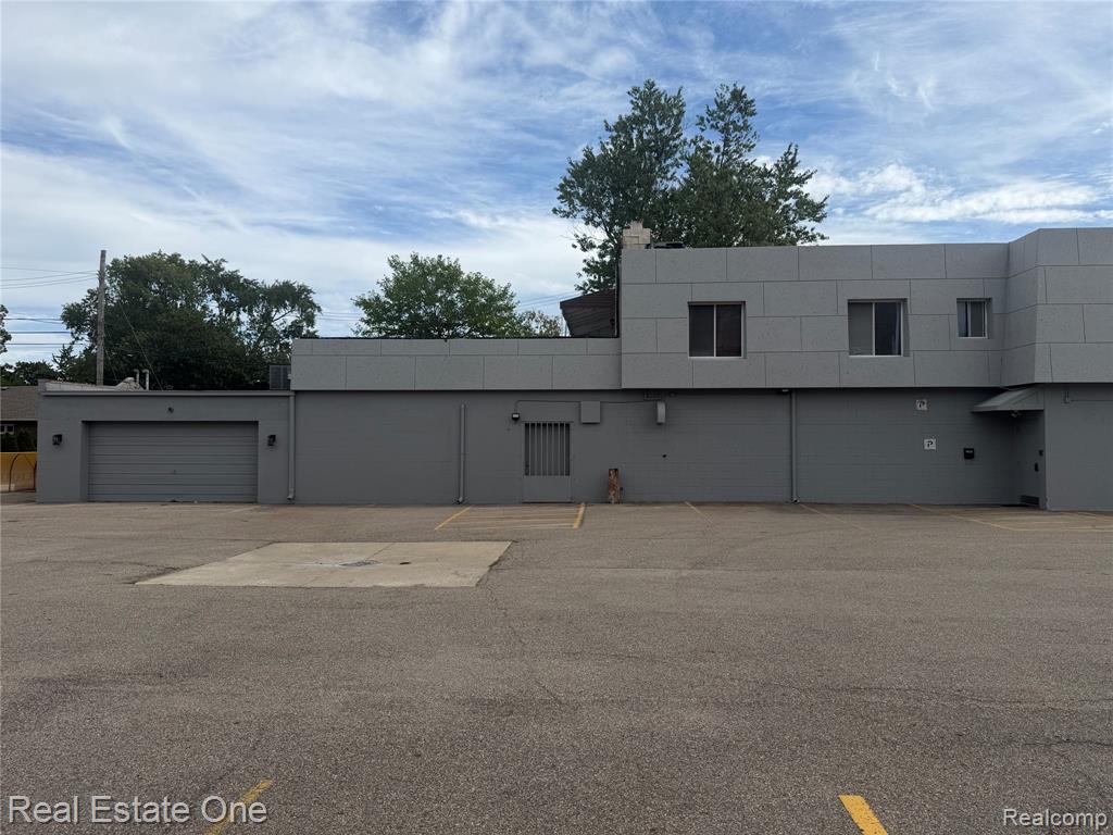 Exterior featuring a modern gray facade, multiple windows, an attached garage, and a large paved lot