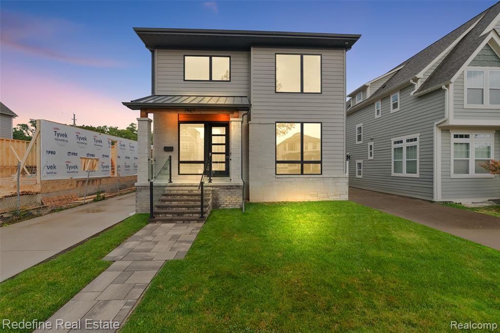 Two-story contemporary exterior with mixed material siding, featuring a covered entry with metal roofing and a glass-paneled front door