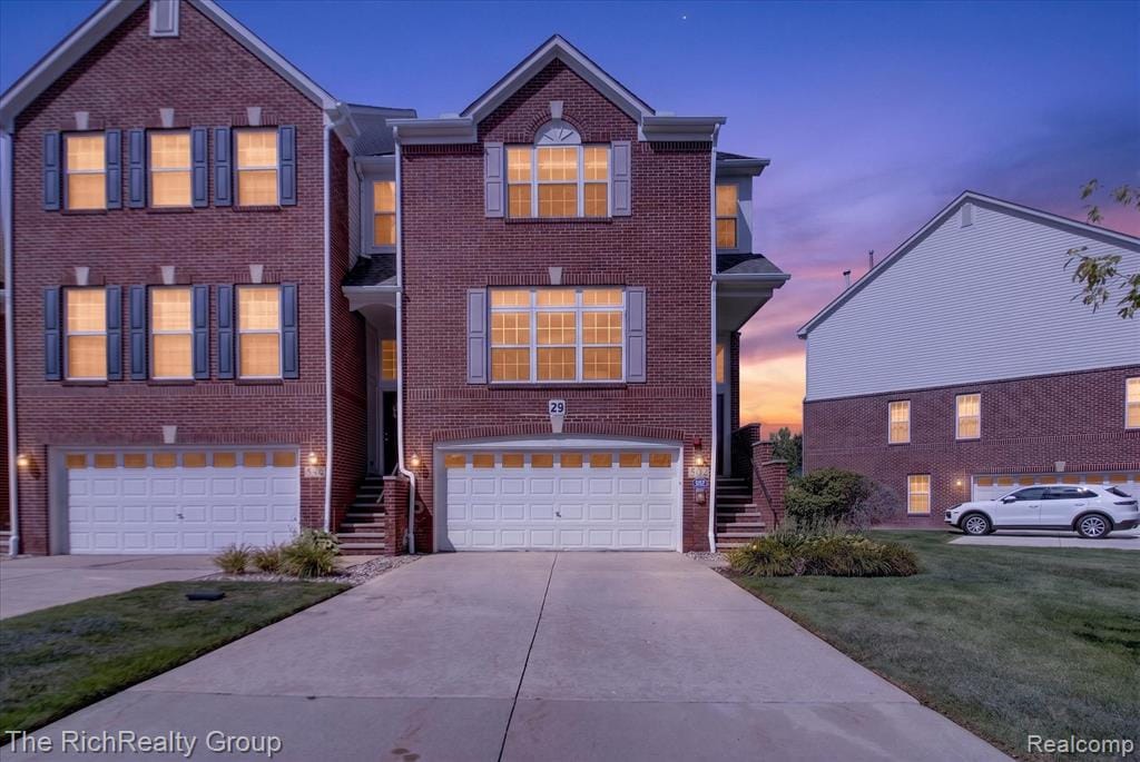 Brick exterior, multiple window shutters, attached garages, paved driveways, and landscaped shrubbery