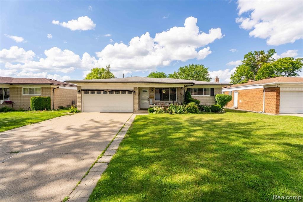 Ranch-style residence featuring a prominent front lawn, an attached garage with a white door, and a concrete driveway