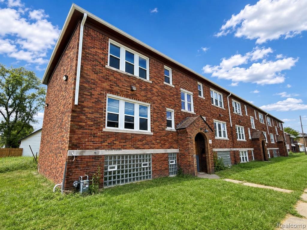 Brick exterior with multiple white-framed windows, a covered entryway, and ground-level glass block windows