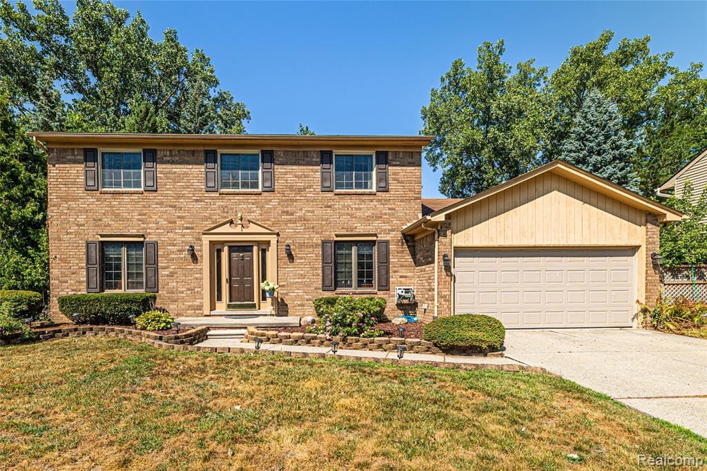 Brick Colonial elevation featuring three upper-level windows, a centered entrance with sidelights, and a two-car attached garage
