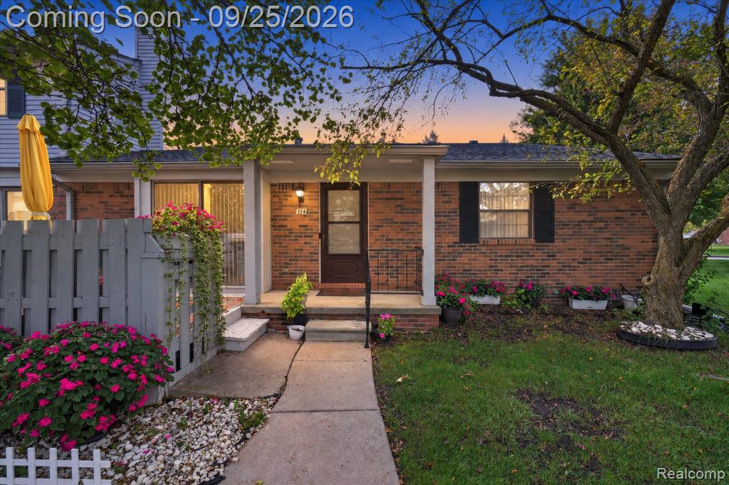 Brick facade with a covered entry, concrete walkway, and established landscaping