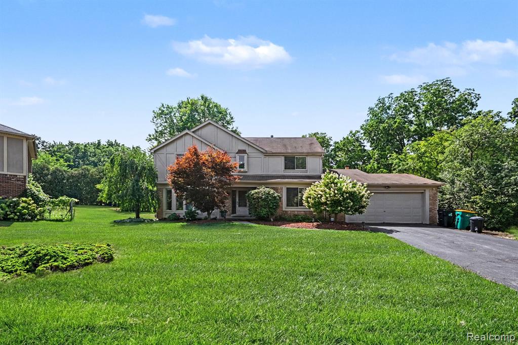 Two-story residence featuring a two-car garage, mature landscaping, and an expansive front lawn