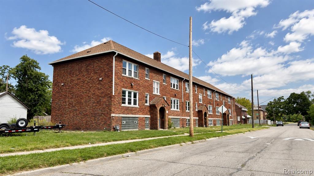Brick multi-unit building featuring multiple entryways with arched surrounds, white-framed windows, and glass block basement windows