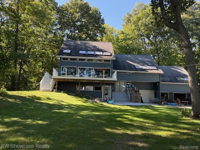 Multi-level exterior with a large second-story deck, extensive glass panel railings, and multiple skylights