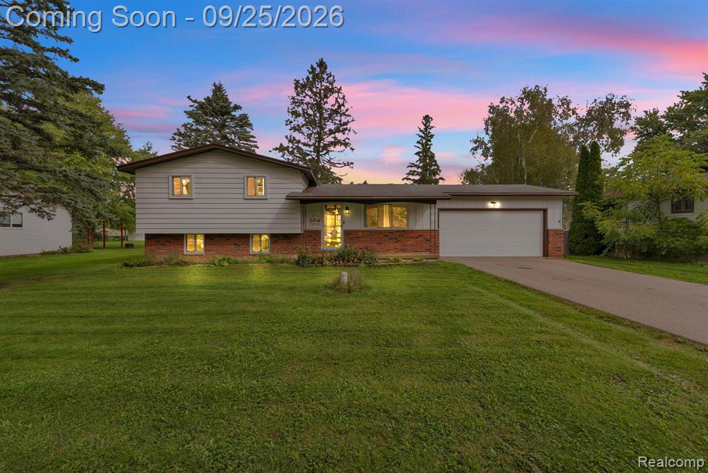 Split-level residence featuring a brick and siding exterior, an attached garage, a paved driveway, and mature landscaping