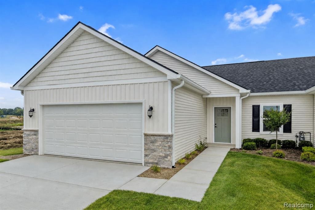 Exterior showcasing a two-car garage, stone veneer accents, light-colored siding, a dark shingle roof, and a pale green front door with a window inset