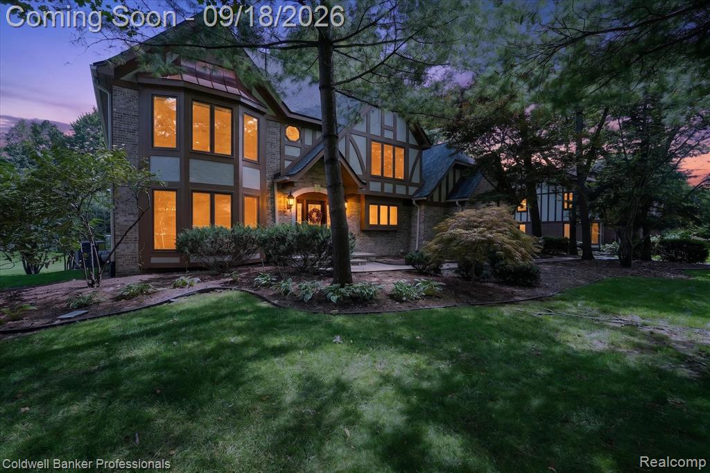 Stately exterior with brick and timber detailing, expansive front lawn, mature trees, and established landscaping