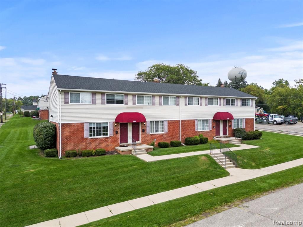 Brick and siding exterior with red awnings and shutters, featuring a dark shingle roof and manicured front lawn