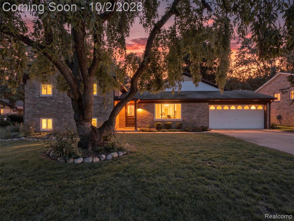 Brick exterior, attached garage, paved driveway, mature tree, stone garden bed border