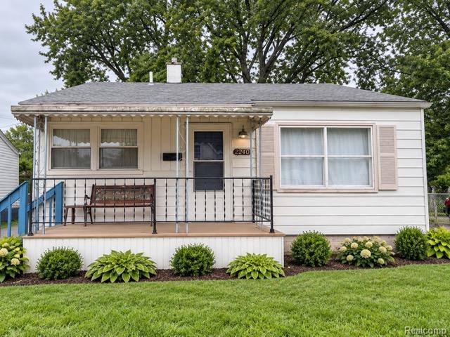 Covered front porch with decorative railing, white siding exterior, and well-maintained shrubs