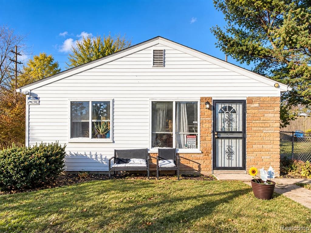 White horizontal siding, brick facade, black security screen door, and a front yard with established landscaping
