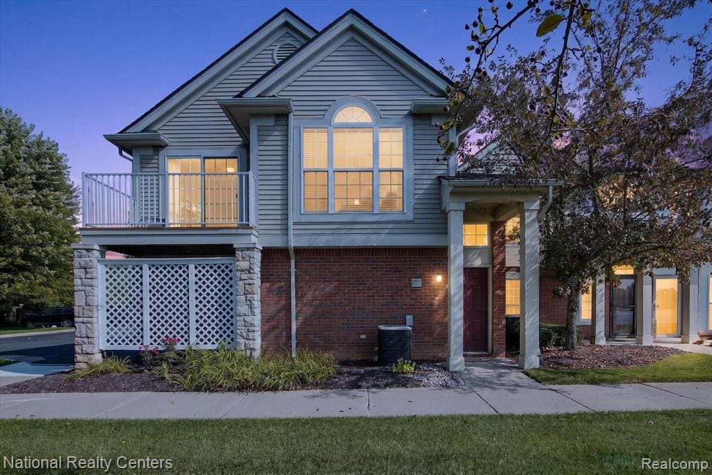 Siding exterior with brick and stone accents, featuring a second-story balcony with metal railing, an arched window, and a covered entry with columns