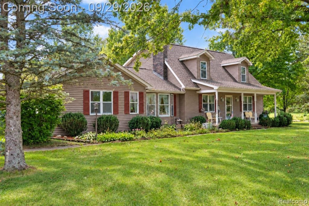 Siding exterior with red shutters, a covered front porch, dormer windows, and a manicured lawn