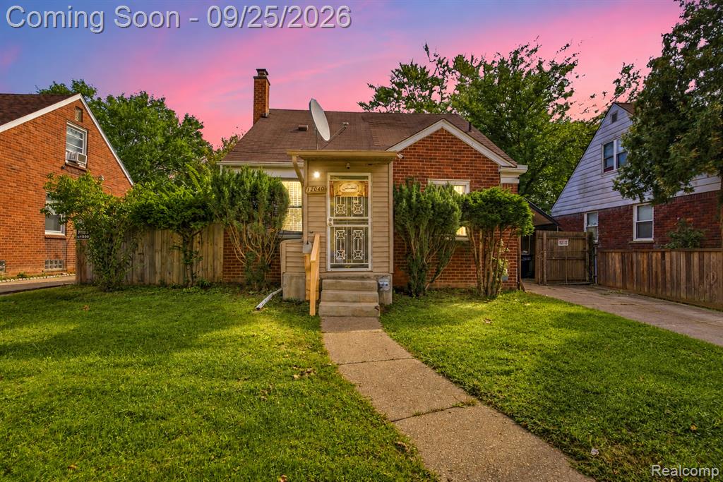 Brick exterior residence with a concrete walkway, established front landscaping, and a wooden privacy fence