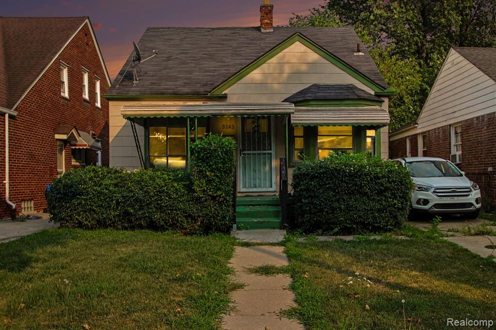 Front exterior featuring a gabled roofline, bay window with awning, covered front entry, and mature front landscaping