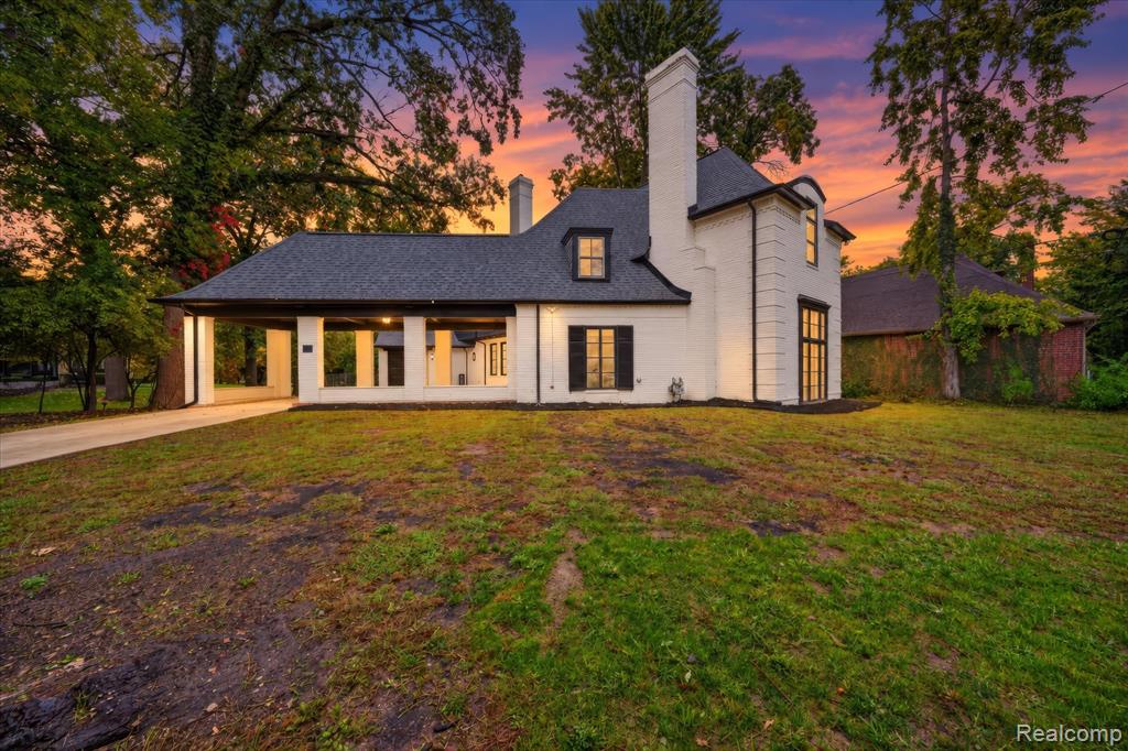White brick exterior with black framed windows, a dark shingle roof, and a prominent chimney feature